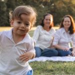 A joyful family enjoying a picnic in the park with a playful toddler in the foreground.