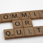 Wooden Scrabble tiles arranged to form the words 'Commit or Quit' on a white background.